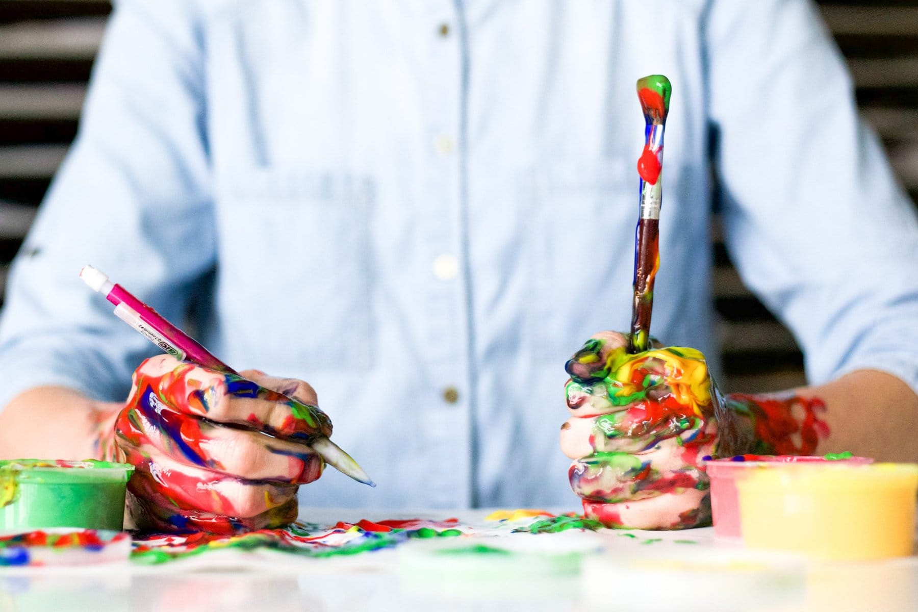 Man's hands covered with paint holding a paintbrush