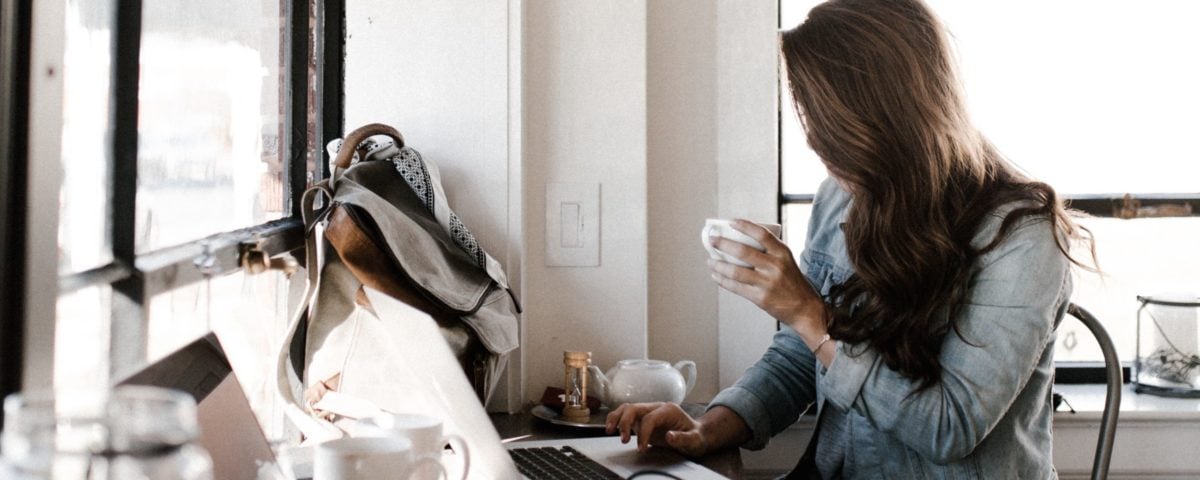 A woman drinking coffee working on her laptop