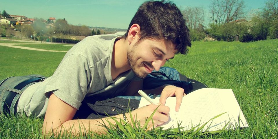 A young man lying on the grass and writing
