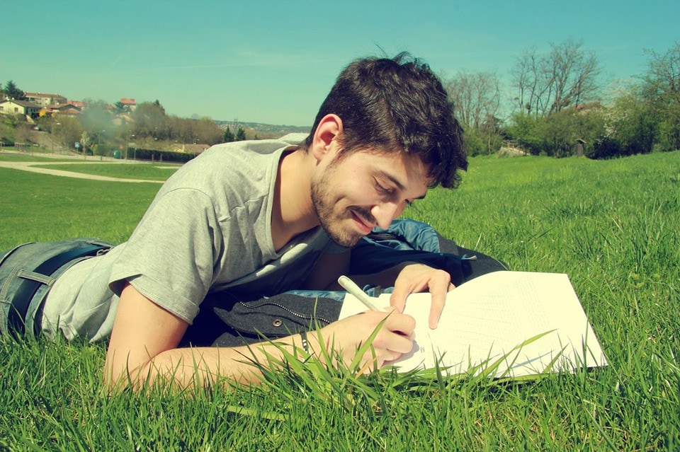 A young man lying on the grass and writing