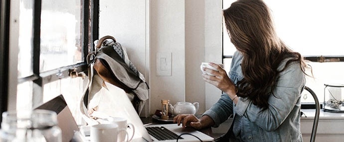 A woman drinking coffee working on her computer