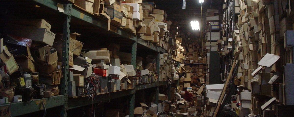 a messy storage room with three shelves of boxes spilling over