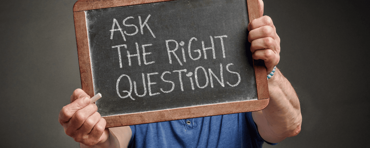 A man holding a small blackboard that reads "ask the right questions"